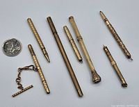 Seven gold-tone vintage pencils of various designs shown with a Canadian quarter for scale, illustrating the overall collection and size differences