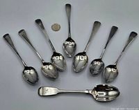 All eight sterling silver spoons arranged with a coin for size comparison, showing variation in size and handle design.