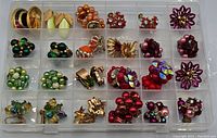 Top-down view of all 18 pairs of vintage clip earrings organized in a transparent plastic box with 24 compartments. The earrings show various designs with colorful faux pearls, enamel, rhinestones, and gold-tone metal.