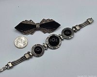 Full view of the onyx brooch and matching bracelet side by side with a quarter for scale.