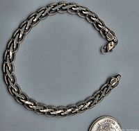 Full view of the sterling silver link bracelet coiled in a loose circle beside a coin for size reference.