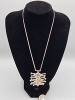 Sterling silver chain displayed on black stand with 2 inch abstract pendant pendant and quarter coin for size reference.