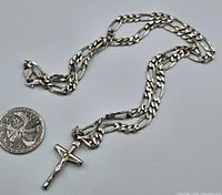 Full view of sterling silver crucifix pendant on figaro chain next to Canadian quarter for scale.