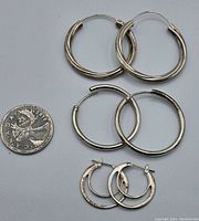 Three pairs of silver hoop earrings laid flat with a Canadian quarter for scale. Earrings vary in size from large to small and show signs of tarnish needing cleaning.