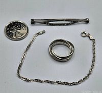 Three sterling silver jewelry pieces including the puzzle ring, bracelet, and brooch alongside a Canadian quarter for scale.