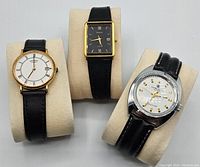 Three wristwatches including a Rotary, Accurist, and Precimax, displayed on beige cushioned stands with black straps visible.