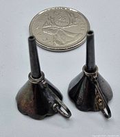 Two small silver miniature funnels standing upright next to a Canadian quarter for size reference. Show size and relative proportions.