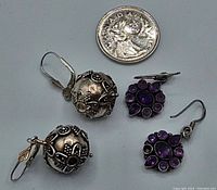 Photo showing both pairs of earrings next to a quarter for scale. Silver ball earrings and purple stone floral earrings are visible, showing size and style.