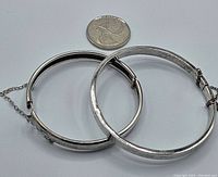 Two vintage silver child-sized bangles shown side by side with a coin for scale, highlighting one smaller engraved with Birks hallmark and the other plain stamped 925.