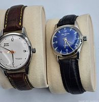 Pair of wrist watches, HMT Janata on left and Henri Sandoz on right, displayed on pads
