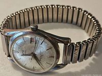 Front angle view of vintage Elco wristwatch showing dial, crown, and stainless steel expandable band with decorative design.