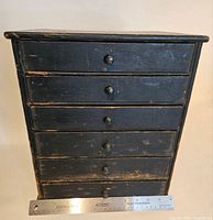 Front view of black-painted wooden cabinet with six drawers, showing wear