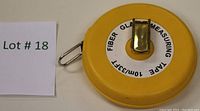 Yellow circular fiberglass measuring tape with metal crank handle on the top and metal clip on the side. The tape length is 10 meters (33 feet) as shown on white label on front.