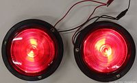 Two round red trailer taillights shown from front lit with light on, showing red lenses and wiring.