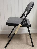 Side view of one folding chair showing black metal frame and grey cushioned seat and backrest with padding on folding joints.