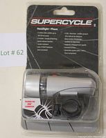 Front view of the Supercycle LED bicycle headlamp in original packaging, showing the silver headlamp and mounting bracket.