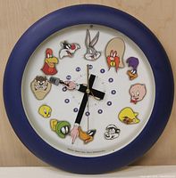 Front view of the clock showing all 12 Looney Tunes character faces positioned as hour markers around the clock face within a blue frame.