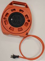 Top down view of orange Noma retractable cord extension cord with outlets and plug end visible.