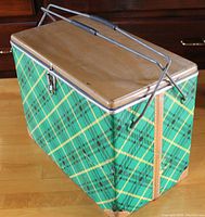 Side view of vintage metal cooler showing green plaid exterior, metal top lid, and foldable metal handle.