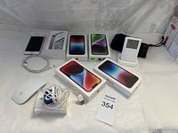 Apple electronic devices on white surface showing iPod Shuffle, iPhones boxes, Magic Mouse, and cables.