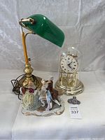 Front wide view of the bankers desk lamp, Elgin clock, and two porcelain figurines arranged on a white surface.