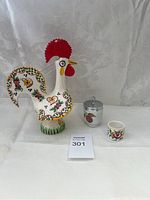 Full view of three items: Portuguese rooster figurine, small container with metal lid, and small ceramic cup on white fabric background