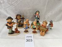 Full collection of 8 Hummel porcelain figurines displayed on white fabric, showing variety of children in playful and musical scenes.