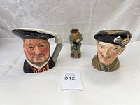 Three items: two Royal Doulton character mugs and one small figurine grouped on white cloth background.