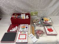 Wide-angle photo of all scrapbooking supplies on display including red basket with floral embellishments, Sizzix die cut sets, ink pads, adhesive, and embellishment packets.