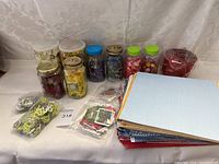 Full view of jars of artificial flower embellishments and stacked scrapbooking papers with packaged embellishments in front.