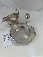 Overall view of silver plate creamer, octagonal tray, and glass bottle with silver lid on white background.