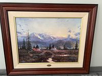 Front view of framed print showing landscape scene of teepees, mountains and trees at sunset with wood outer frame and linen mat.