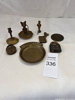 Full view of all vintage bronze items laid out on white surface including figurines, dish, locks, corkscrew, and bell