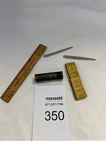 Photo of sewing accessories including wooden ruler, sewing needles, tape measure, and Victoria container