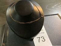 Thin gold chain necklace displayed on black jewelry bust.