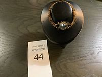 Gold tone bracelet displayed on a black round holder, showcasing the overall design and condition.