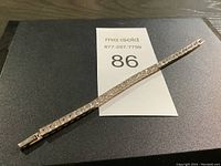 Full length view of silver metal link bracelet on black surface with lot number card.