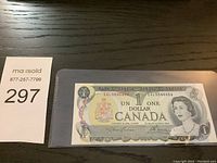 Photo showing front side of used Canadian one dollar bank note in protective sleeve, serial number EAL354U4606 clear, including Queen Elizabeth II portrait and Bank of Canada crest.