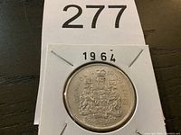 Front view of the 1964 Canadian half dollar coin in cardboard holder showing the coat of arms.