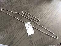 Two silver chains laid out on a wooden surface, showing entire length and clasp details.