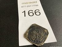 Close up of hexagonal coin with detailed eagle crest and inscriptions, showing surface wear and patina.