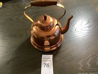 Photo showing the full copper kettle with wooden handle and curved spout on a black surface, highlighting overall shape and condition.