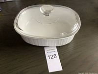 White oval Corning French ceramic baking dish with clear glass lid and round knob on top, shown from side angle