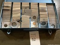 Metal storage tray filled with rows of white cardboard flips, each holding an individual coin, sorted by date
