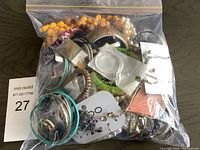 Bag of assorted costume jewelry including bracelets, necklaces, and earrings in mixed materials and colors.