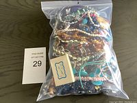 Clear plastic bag containing assorted costume jewellery items including beads, chains, and a small box on wooden surface