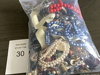 Clear plastic bag filled with assorted estate costume jewelry, showing beads and various metal jewelry pieces inside.