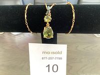 Full view of the gold-tone chain necklace with pendant displayed on black jewelry holder with lot number card.