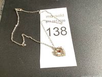 Full view of silver chain necklace with heart-shaped pendant featuring clear stones and a red center stone, laid on a black surface.