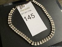 Full view of the clear stone necklace laid flat against a black surface with the lot number tag visible.